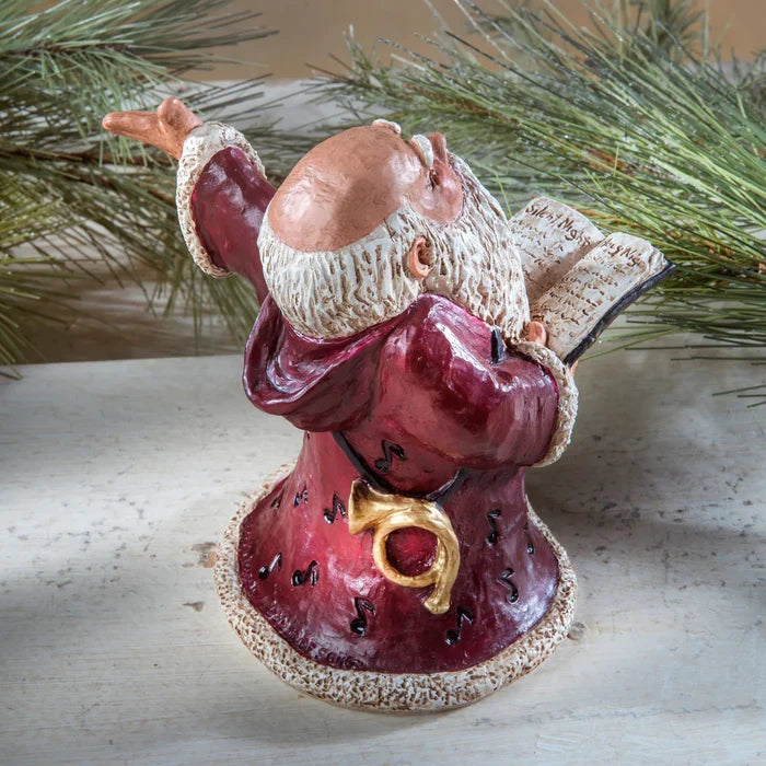 Decorative figurine of a Santa in a red outfit with a gold bow, against a natural background.