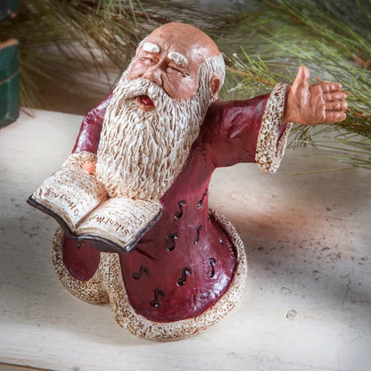 Decorative figurine of Santa with a beard, wearing a red robe, holding a book.
